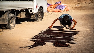 Person cleaning dark liquid spilled on dusty road.